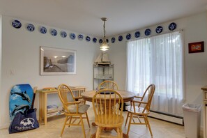 Un coin repas est aménagé avec une table ronde en bois et quatre chaises, une bibliothèque, un tableau encadré et une assiette décorative qui orne le mur.