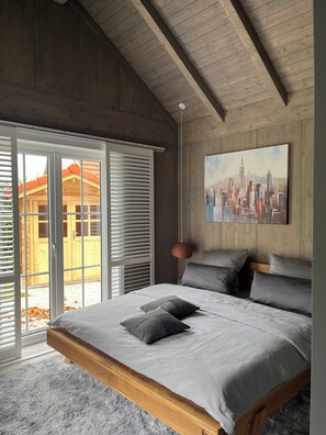 Ein Schlafzimmer mit einem großen Bett, Holzbalkendecke, einem Stadtbildgemälde und Blick aus dem Fenster.
