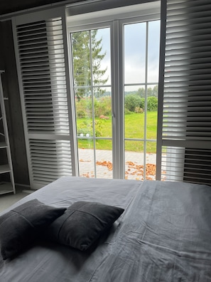 A bedroom with a bed, a wardrobe, and a view of a garden through a sliding glass door. - Roosisaar – Lake Views, Tranquility, and Wild Geese on Lake Grand Tessin (Groß Tessin)