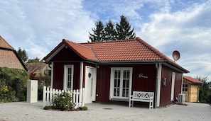 Ein rotes Holzhaus mit einem Ziegeldach, einem weißen Zaun und einer Bank davor.