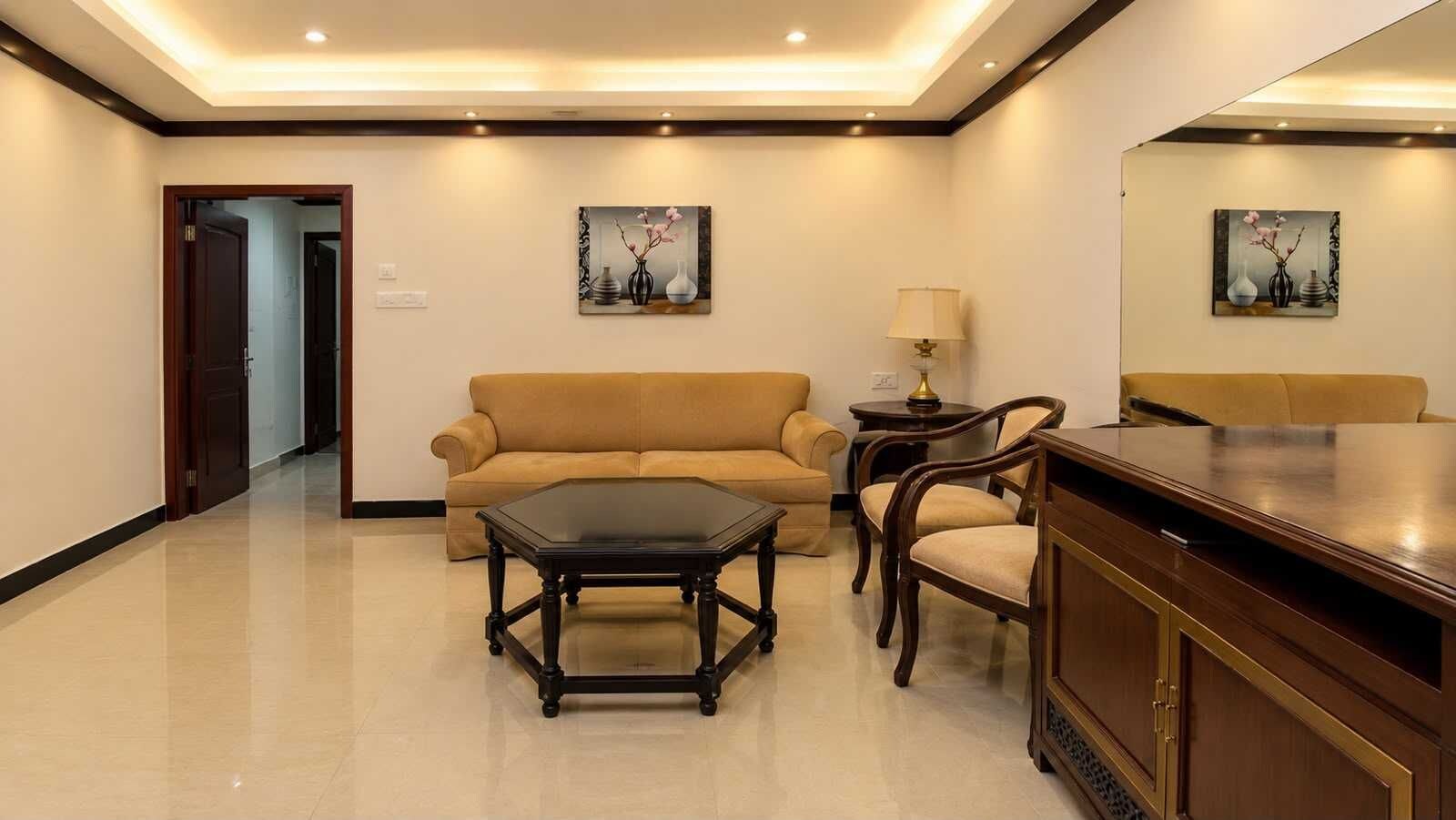 A hotel room with a sofa, a table, chairs, a lamp, and artwork on the walls.