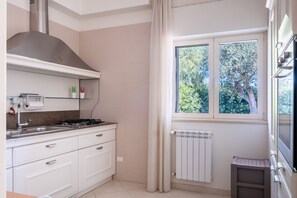 A modern kitchen with a gas stove, white cabinets, a window with a view of trees, and a radiator. - Villa Andrews by Wonderful Italy (Bari)