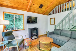 A living room with a fireplace, a television, a sofa, a chair, and a staircase. - Lake Cushman Cabin - Hike, Swim, Golf, Relax (Hoodsport)