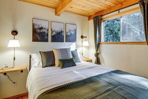 A bedroom with a bed, two bedside tables, a window with curtains, and three framed pictures on the wall. - Lake Cushman Cabin - Hike, Swim, Golf, Relax (Hoodsport)