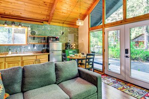 A cozy interior with a sofa, kitchen area, and large windows offering a view of the outdoors. - Lake Cushman Cabin - Hike, Swim, Golf, Relax (Hoodsport)