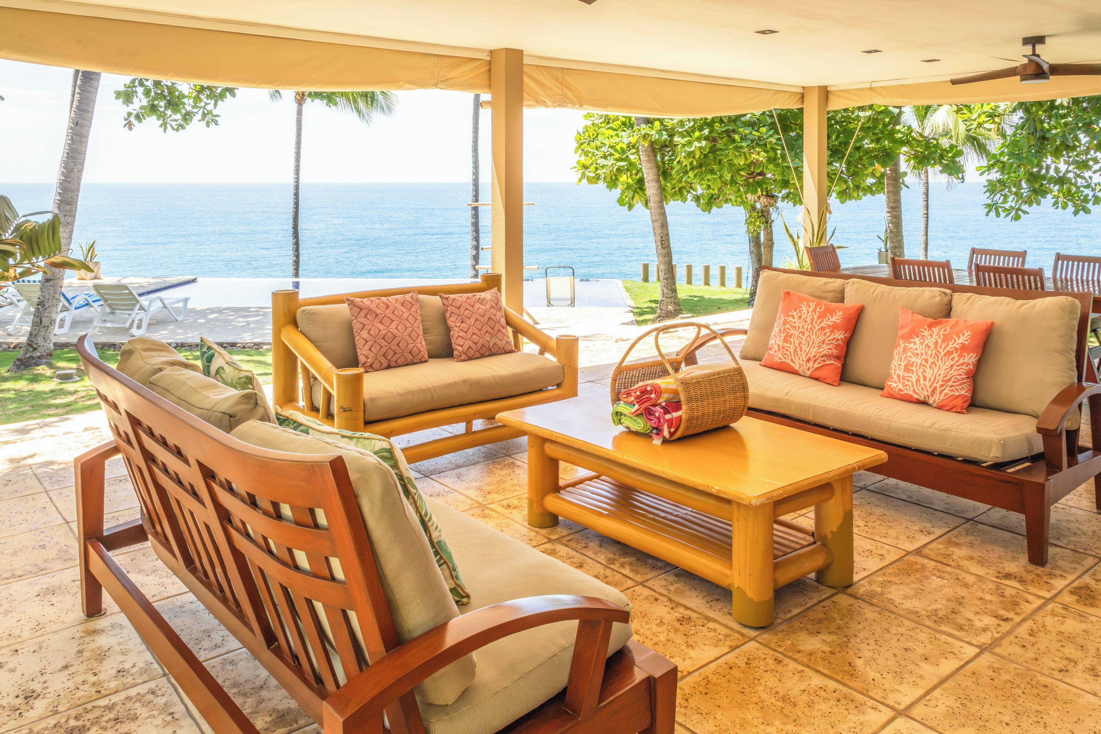 A covered outdoor seating area with wooden furniture and a view of the sea.