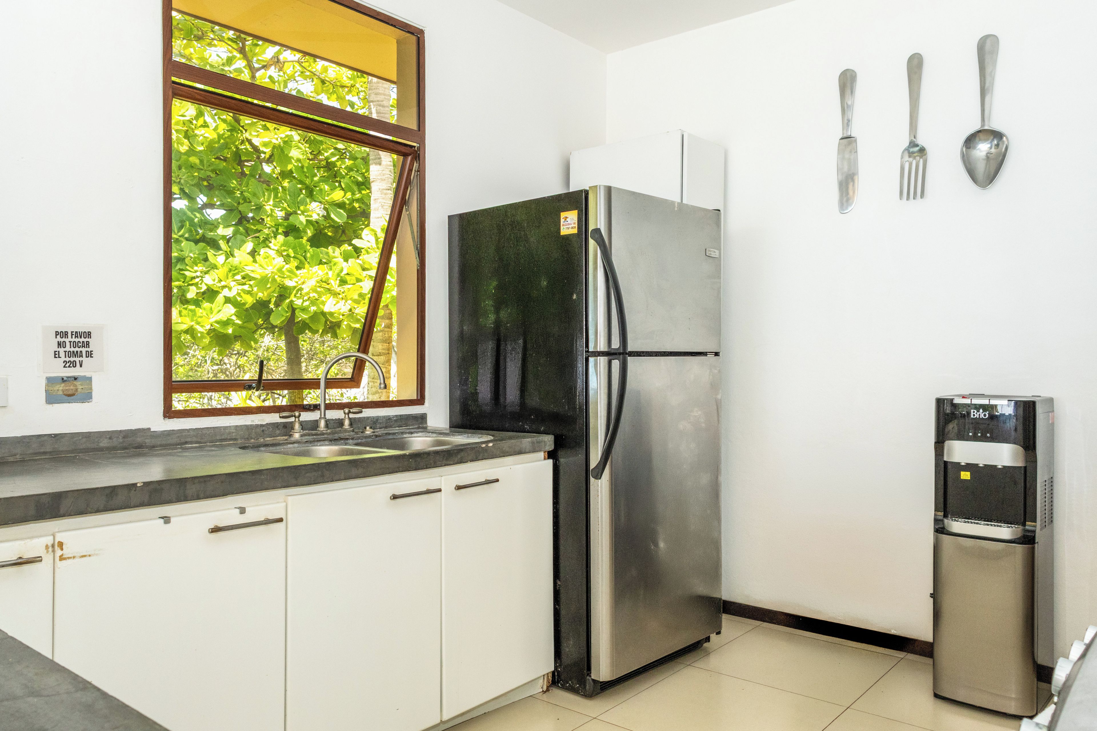 Una cocina con un refrigerador de acero inoxidable, un dispensador de agua y una ventana con vistas a árboles.