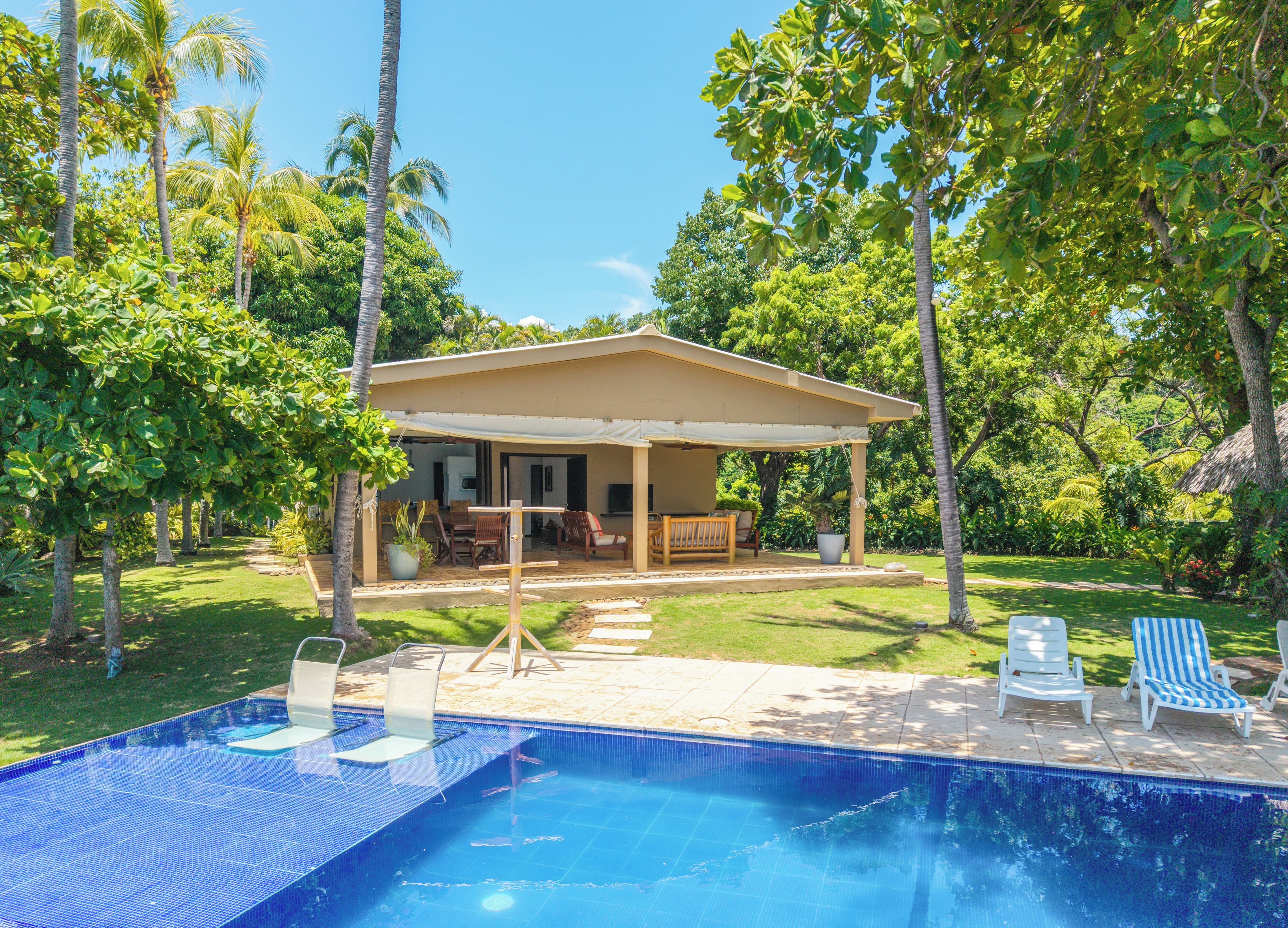 A pool area with a covered seating area, lounge chairs, and a clear blue pool.