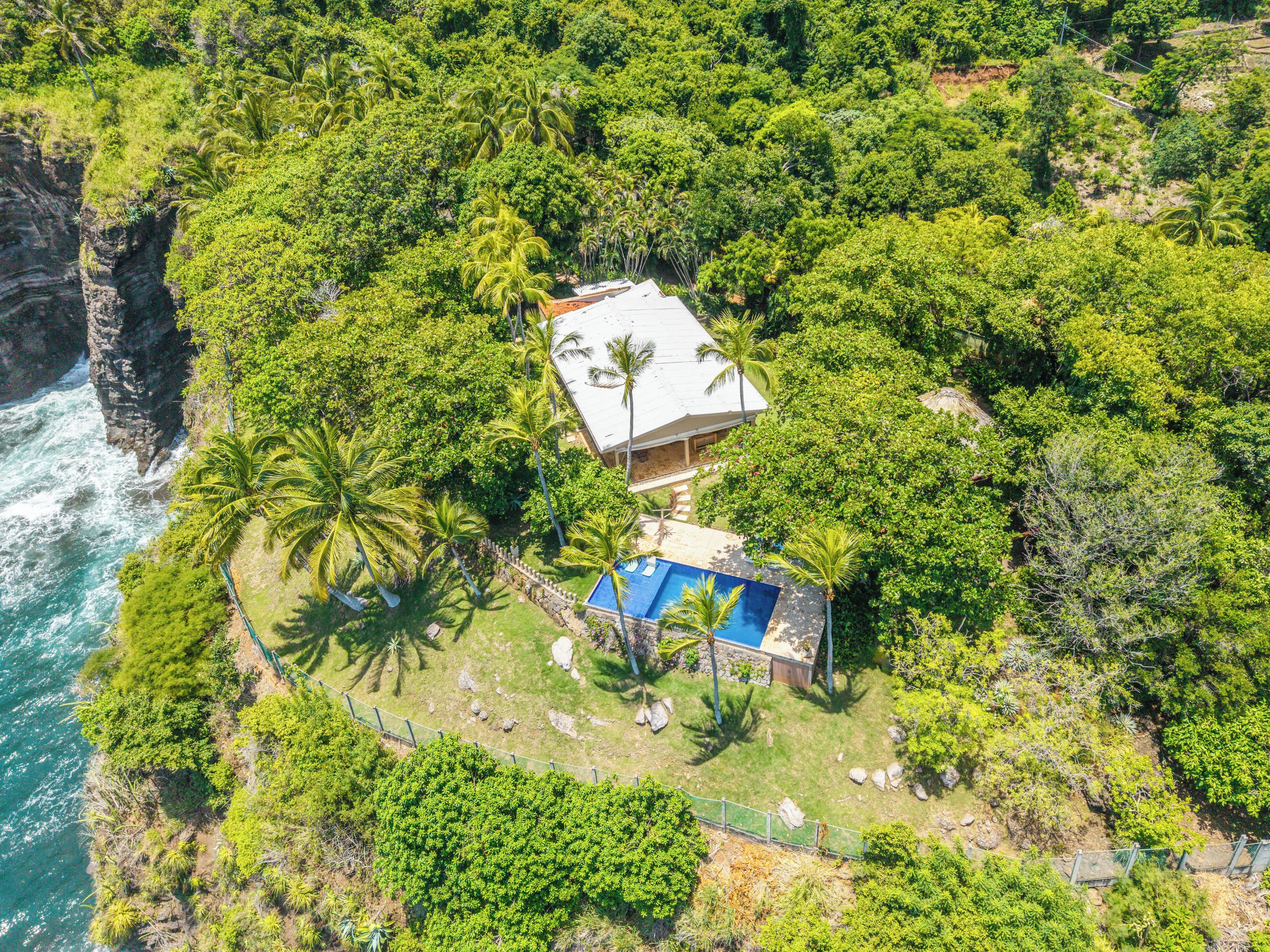 A coastal property with a swimming pool, surrounded by lush greenery and a cliff overlooking the ocean.