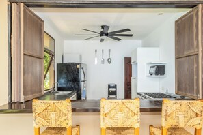 A kitchen with a refrigerator, microwave, and coffee maker. There are three woven chairs and a ceiling fan. - Casa en el Risco (Taquillo)