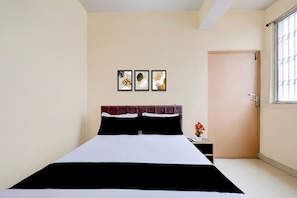Una habitación de hotel con cama, mesita de noche, una puerta y tres cuadros colgados en la pared.