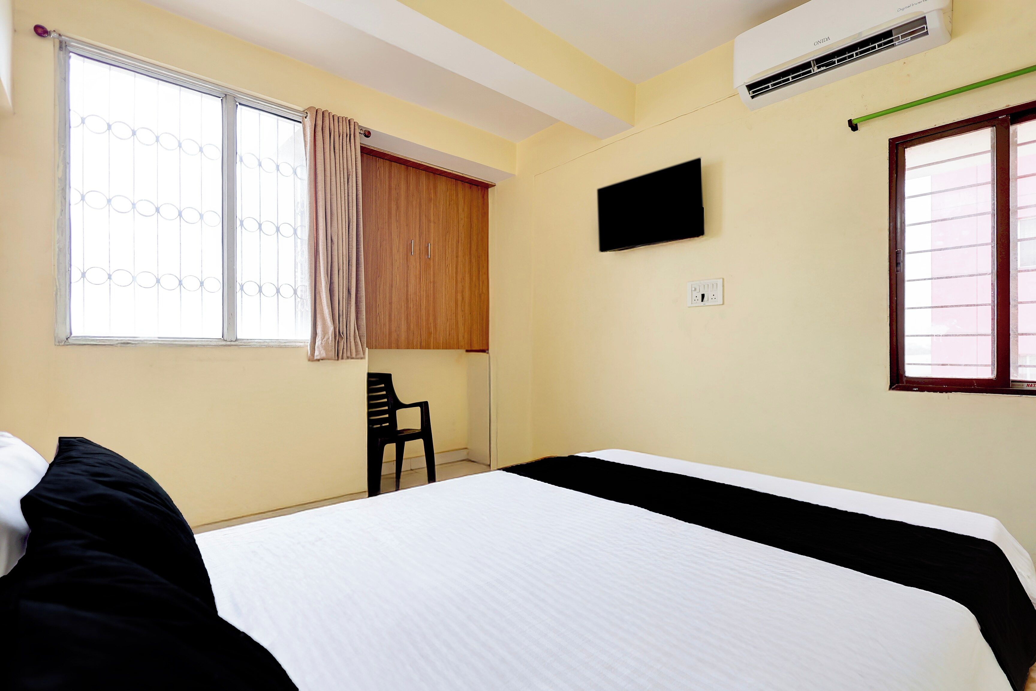 A bedroom with a bed, a chair, an air conditioning unit, a TV, and a window with curtains.