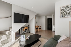 A modern living room with a flat-screen TV, a dining area with a table and chairs, and a staircase leading to another level. - Central Stay – 5 Min Walk to Te Pae + FREE Parking (Christchurch)