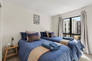 A hotel room with two beds, a bedside table with a lamp, and a window with curtains. - Central Stay – 5 Min Walk to Te Pae + FREE Parking (Christchurch)