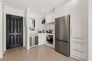 A modern kitchen with white cabinetry, stainless steel appliances, and a black door. - Central Stay – 5 Min Walk to Te Pae + FREE Parking (Christchurch)