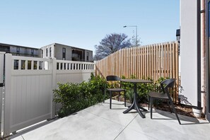 An outdoor patio with a table and chairs, a white fence, and a wooden fence in the background. - Central Stay – 5 Min Walk to Te Pae + FREE Parking (Christchurch)