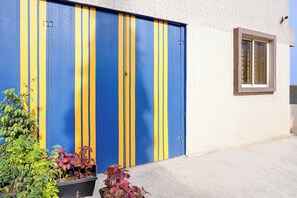 A building with a blue and yellow striped garage door, a window with a brown frame, and potted plants in the foreground. - Hotel O Ambedkar Nagar Bus Terminal (Bengaluru)
