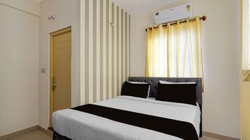 Un dormitorio con cama, papel tapiz a rayas, una ventana con cortinas amarillas y un equipo de aire acondicionado.