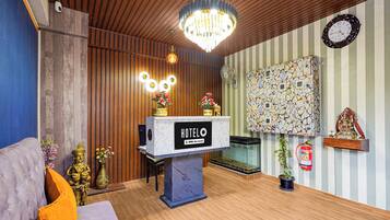 Área de recepção de hotel com teto de madeira, um lustre, balcão de recepção e relógio fixado na parede.