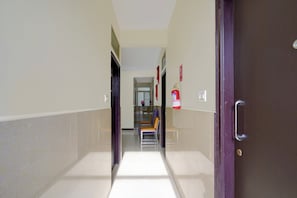 A hallway with a fire extinguisher mounted on the wall, a door with a handle, and a bench with a towel draped over it. - Hotel O Ambedkar Nagar Bus Terminal (Bengaluru)