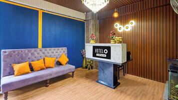 A hotel reception area with a purple sofa, a chandelier, and a sign that reads 'HOTEL OYO-Serviced'.