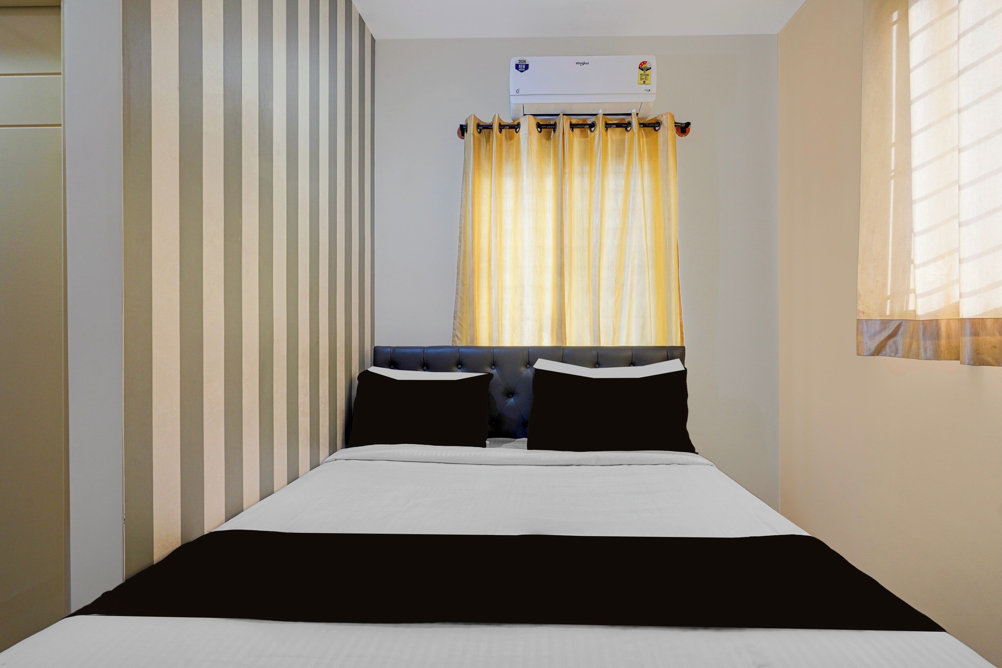 Une chambre d’hôtel avec un lit, une fenêtre avec des rideaux, un climatiseur fixé au mur et un mur à rayures.