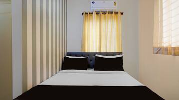 Une chambre d’hôtel avec un lit, une fenêtre avec des rideaux, un climatiseur fixé au mur et un mur à rayures.