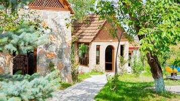 A stone building with a tiled roof, a pathway leading to it, and a tree in the foreground.