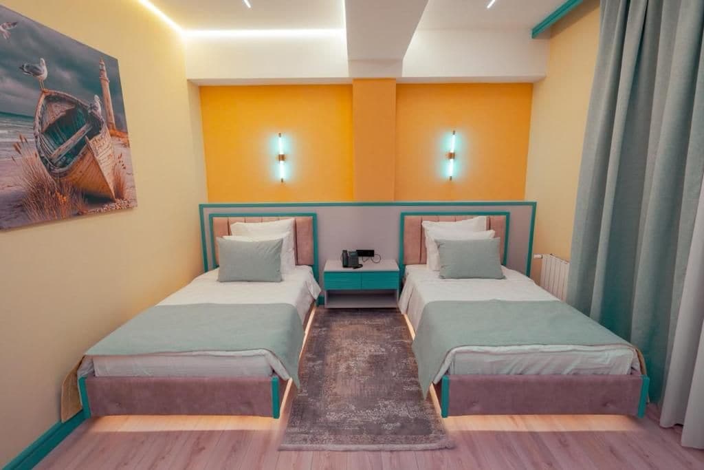 A hotel room with two beds, a small table, and a painting on the wall.