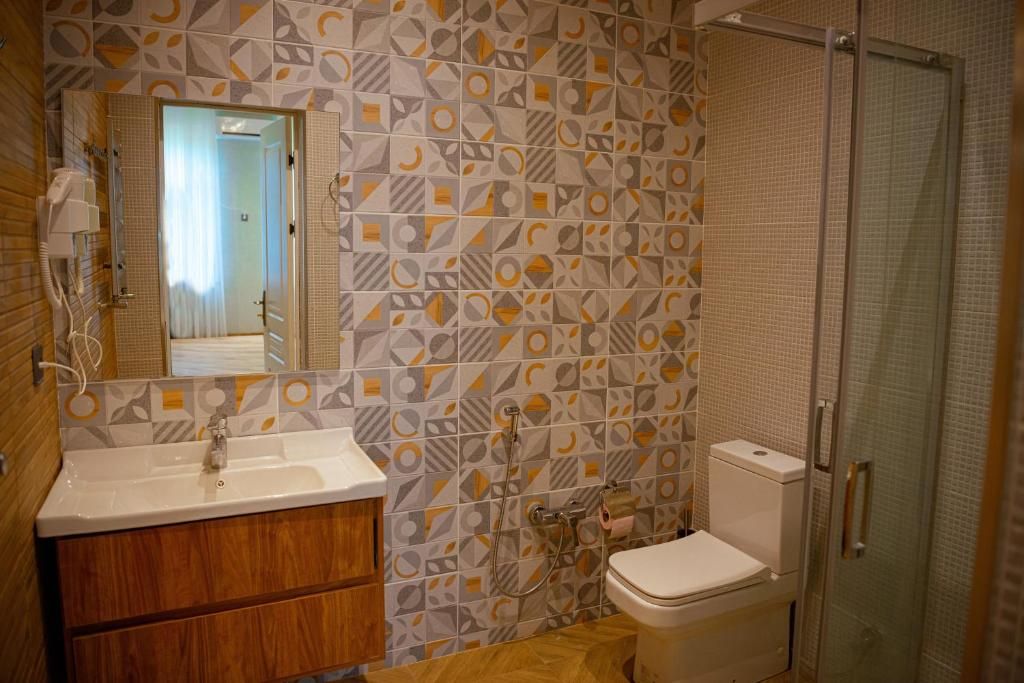 A bathroom with a geometric patterned wall, a wooden vanity, a white sink, a toilet, and a glass shower enclosure.