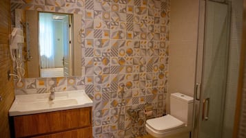 A bathroom with a geometric patterned wall, a wooden vanity, a white sink, a toilet, and a glass shower enclosure.