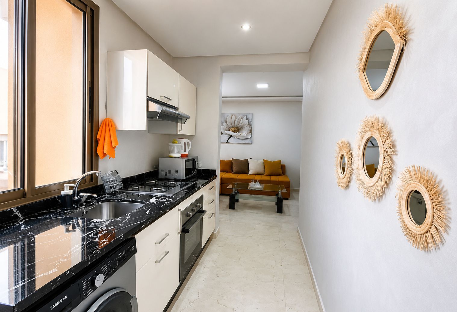 A compact kitchen with a dishwasher, microwave, and stove. There is a sofa and a painting in the living area.