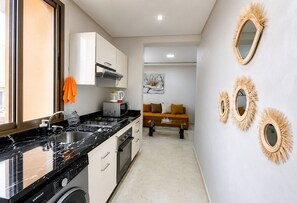 Cocina compacta con lavavajillas, microondas y estufa. Hay un sofá y un cuadro en la sala.