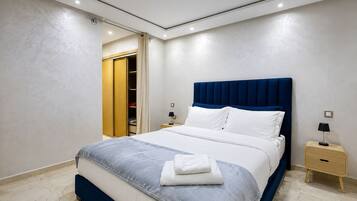 Un dormitorio moderno con cama, mesitas de noche, un armario y la puerta del baño.