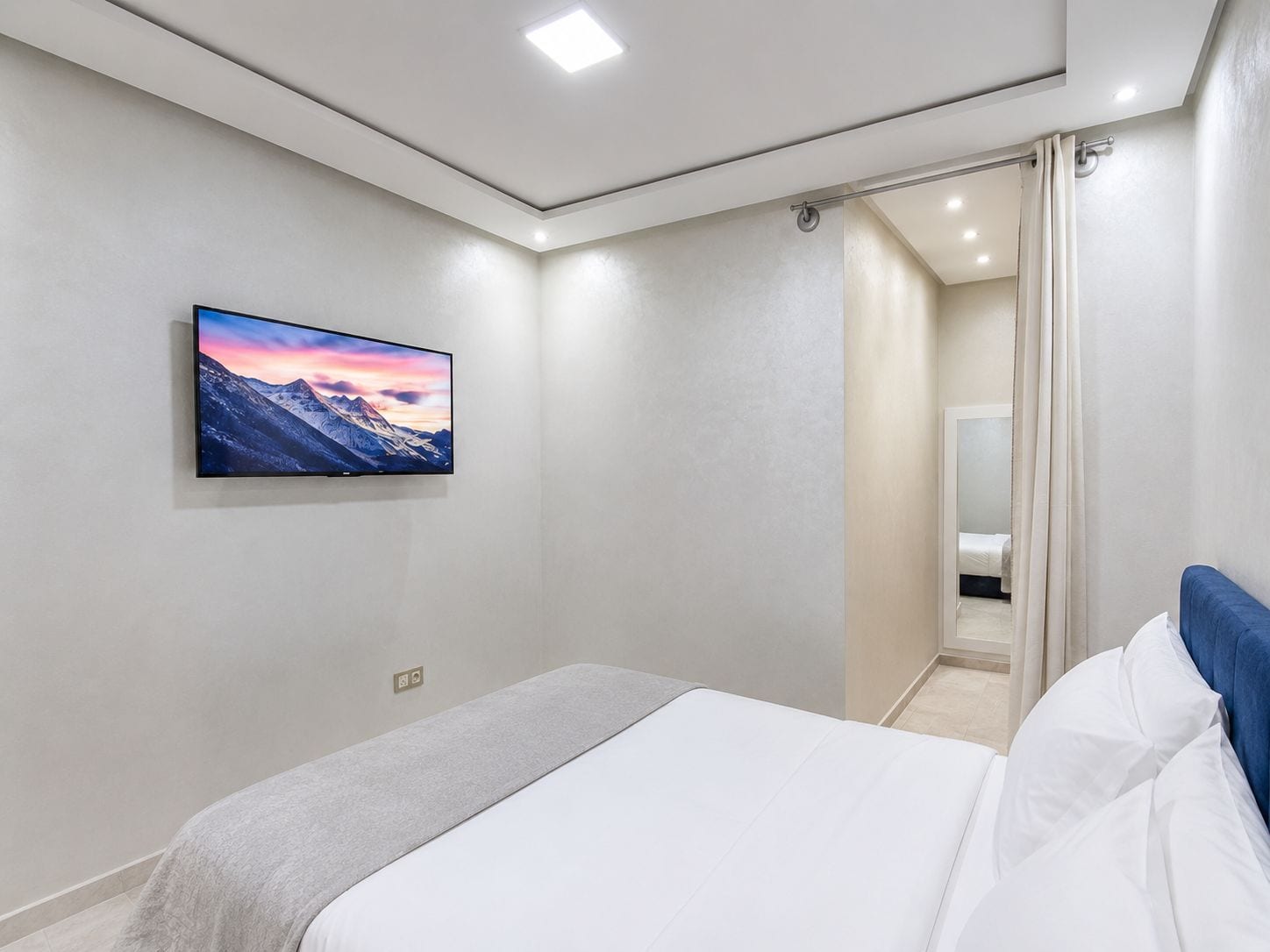 Un dormitorio con cama, televisor montado y baño visible a través de una puerta.