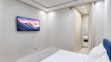 Un dormitorio con cama, televisor montado y baño visible a través de una puerta.
