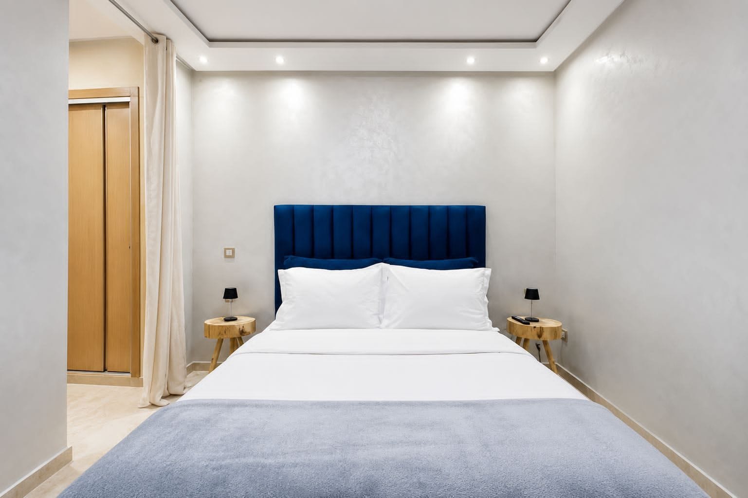 Una habitación de hotel con una cama grande, un cabecero azul, dos mesitas de noche con lámparas y un armario de madera.
