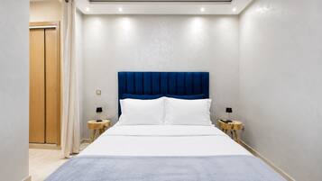 Una habitación de hotel con una cama grande, un cabecero azul, dos mesitas de noche con lámparas y un armario de madera.