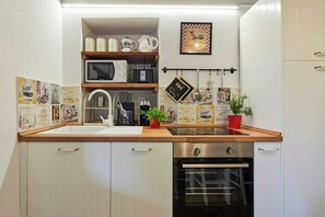 A kitchen with white cabinetry, a stainless steel oven, a microwave, and a coffee machine. There are decorative coffee-themed tiles on the wall and a small potted plant on the counter. - Apartment with terrace over Umbrian countryside (Gubbio)