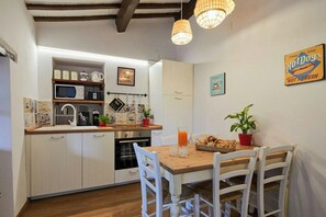 A compact kitchen with white cabinetry, a microwave, and a dining area with a wooden table and white chairs. - Apartment with terrace over Umbrian countryside (Gubbio)