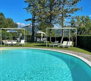 A swimming pool with clear water, surrounded by white lounge chairs and umbrellas, set against a backdrop of trees and mountains. - Apartment with terrace over Umbrian countryside (Gubbio)