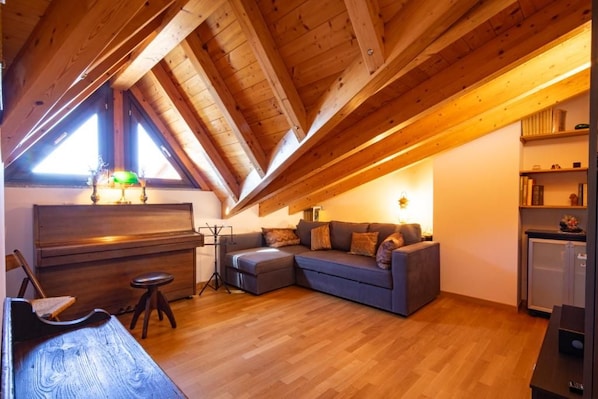 Quarto em estilo loft com teto de madeira, um piano, um sofá e uma mesa pequena.