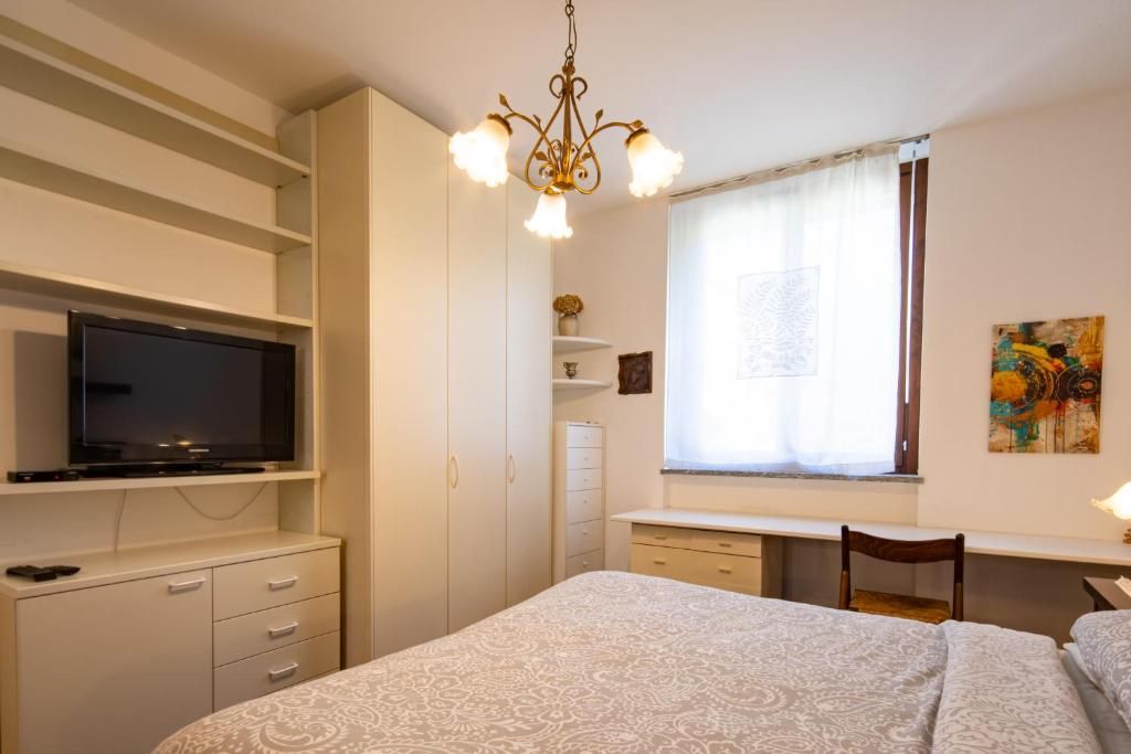 Ein Schlafzimmer mit einem Bett, einem an der Wand befestigten Fernseher, einem Schreibtisch mit Stuhl und einem fenster mit Vorhängen.