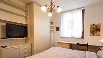 Ein Schlafzimmer mit einem Bett, einem an der Wand befestigten Fernseher, einem Schreibtisch mit Stuhl und einem fenster mit Vorhängen.