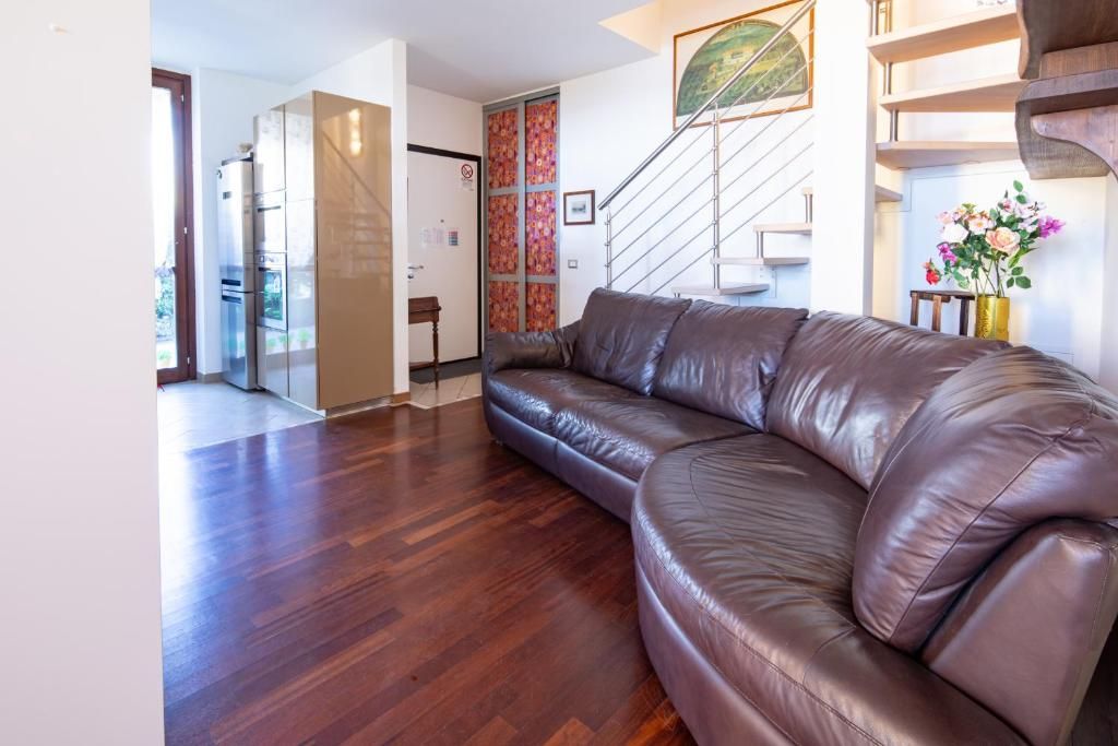 Ein modernes Wohnzimmer mit Ledersofa, Holzboden, einer Treppe und einem Kühlschrank.