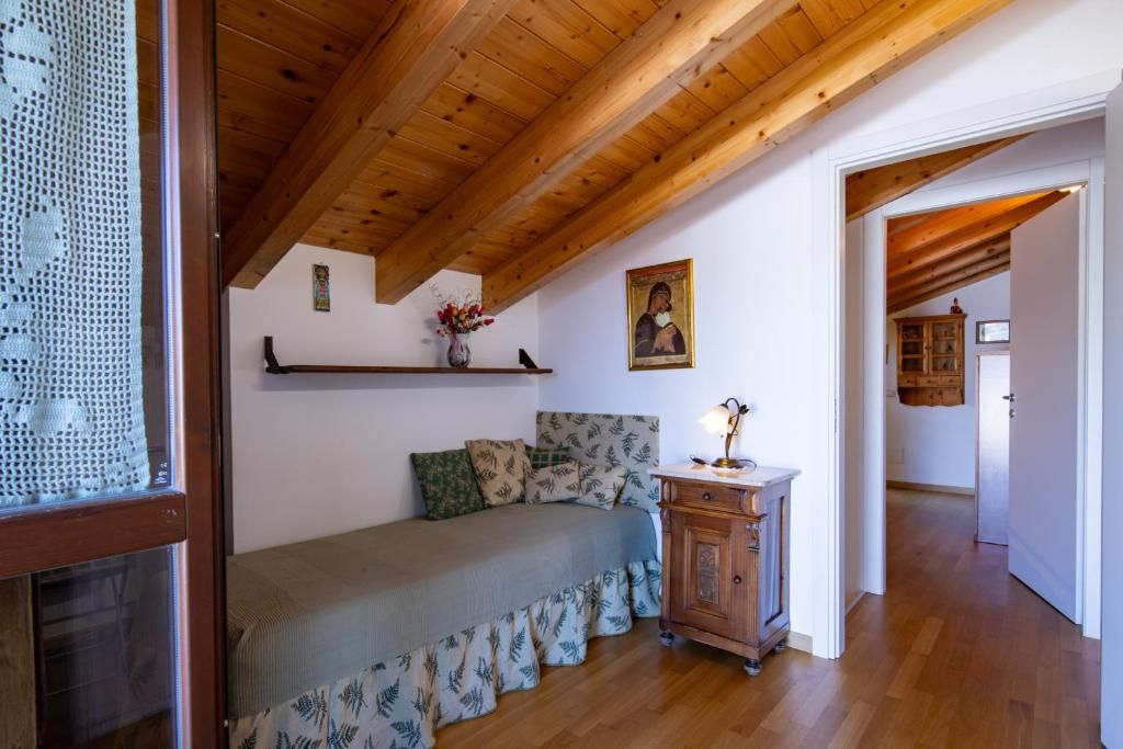 Une chambre avec un plafond en bois, un lit avec une literie à motifs, une table de chevet avec une lampe et un tableau accroché au mur.