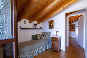 A bedroom with a wooden ceiling, a bed with patterned bedding, a nightstand with a lamp, and a painting on the wall.