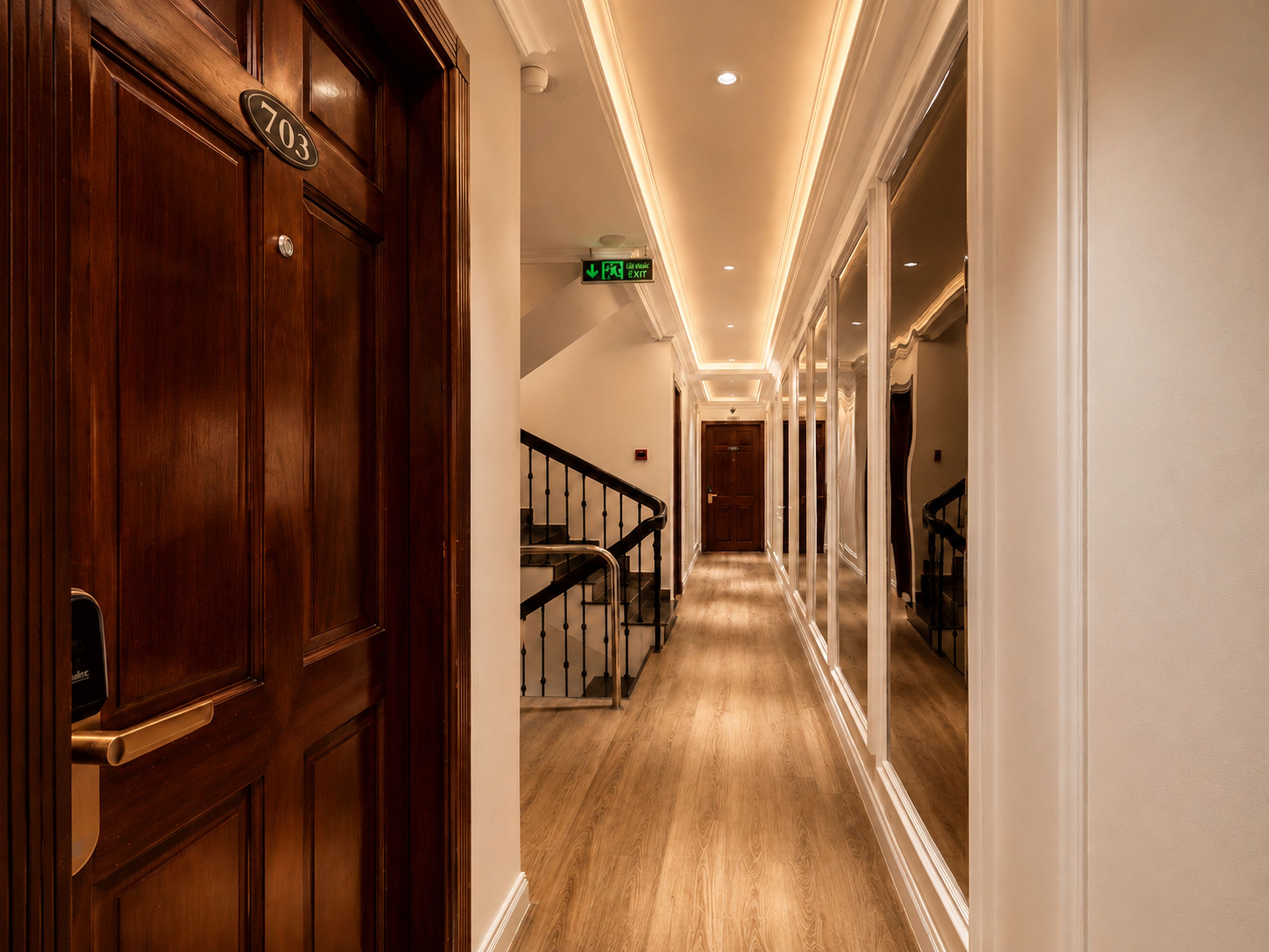 A hallway with a wooden door marked '703', a staircase with a handrail, and a sign indicating an exit.