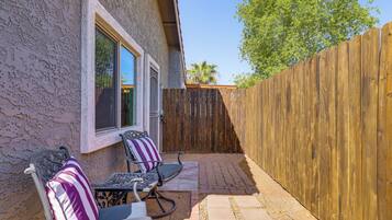 Un patio con due sedie e un tavolo, una recinzione in legno e una casa con pareti intonacate.