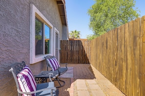 Un patio con dos sillas y una mesa, una valla de madera y una casa con paredes de estuco.